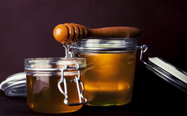 Frasco de miel de abeja con un panal y una cuchara de madera